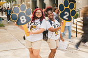 Two students holding up paw prints for a sports game